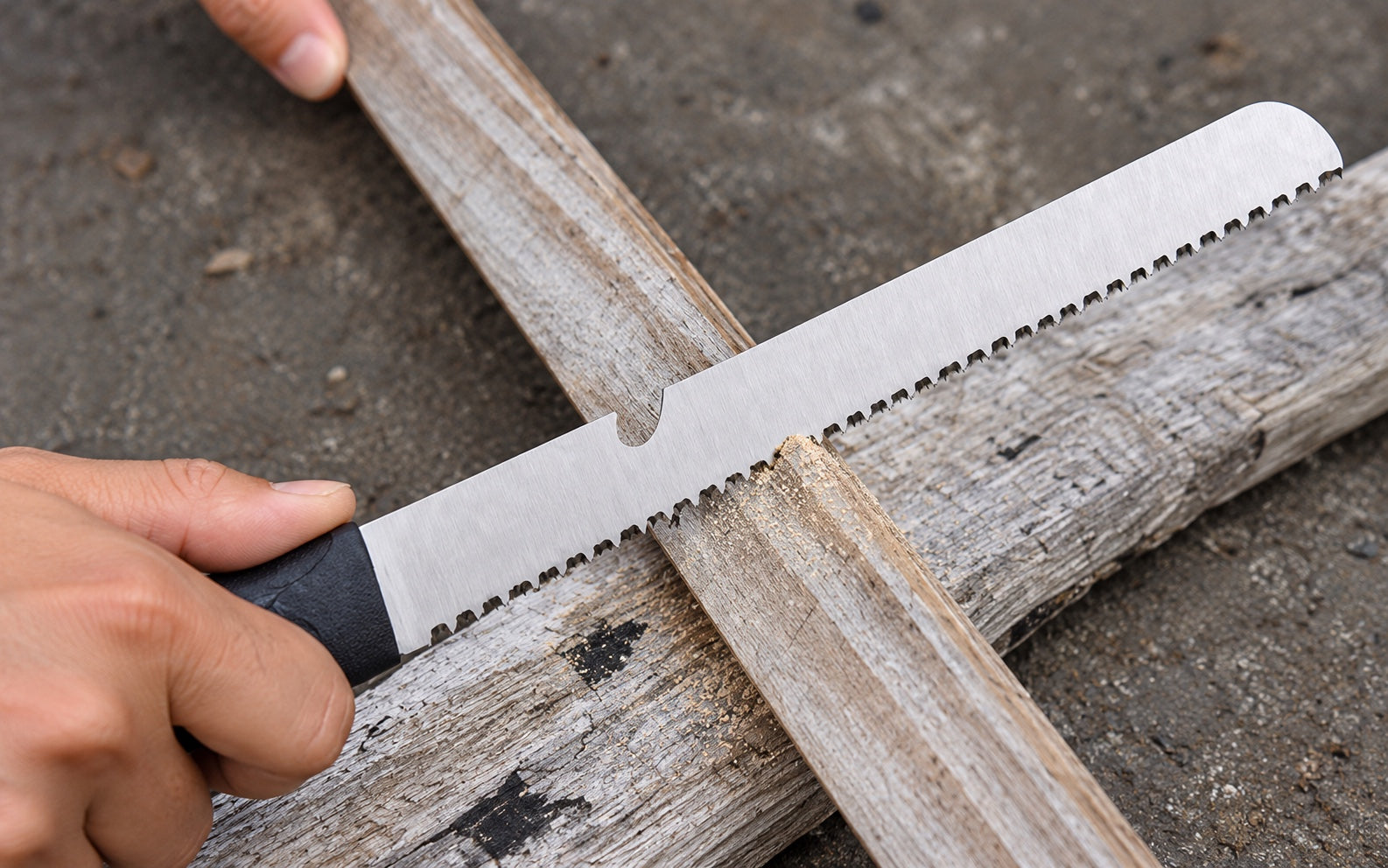 The removable serrated blade sawing through a small piece of wood